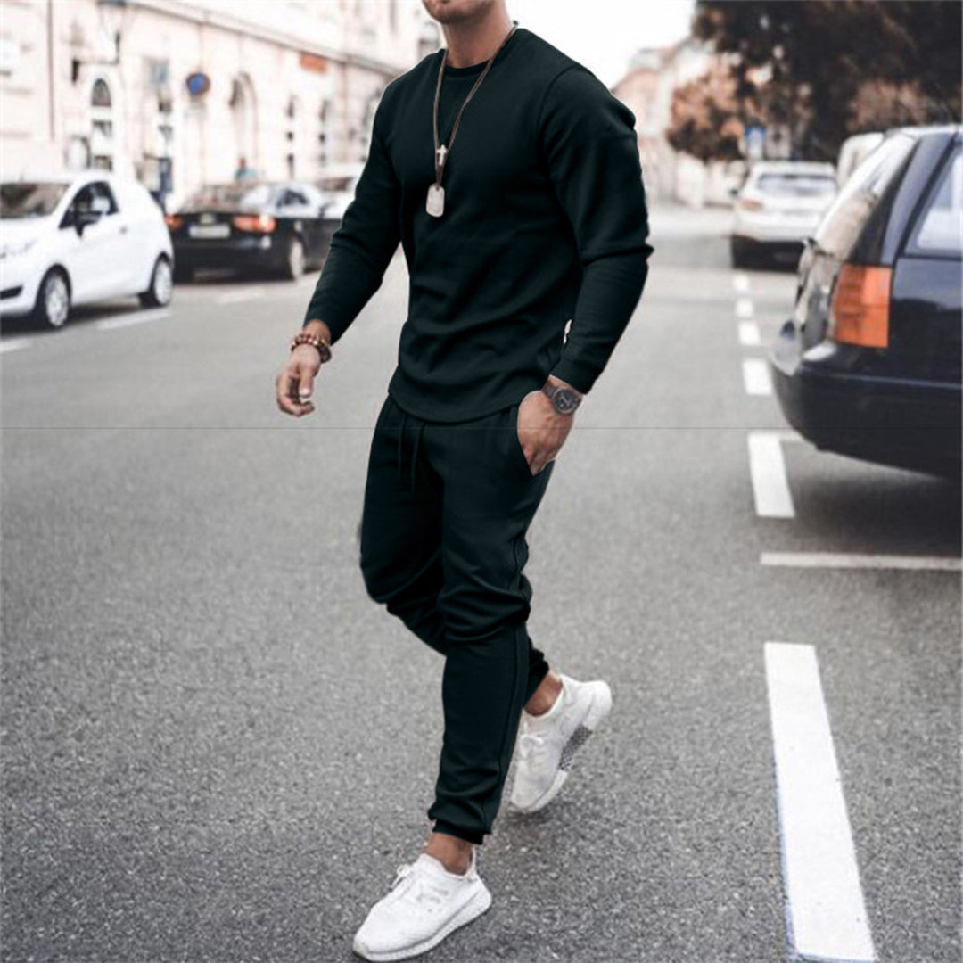 Man in zwart trainingspak en witte sneakers loopt op straat; modieuze herenkleding, casual sportieve outfit, stedelijke stijl.
