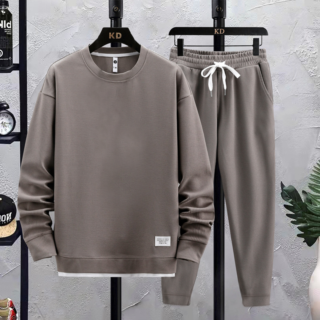 Grijs heren joggingpak, bestaande uit een trui en joggingbroek, ideaal voor sport en casual wear. Comfortabel, stijlvol en trendy design.