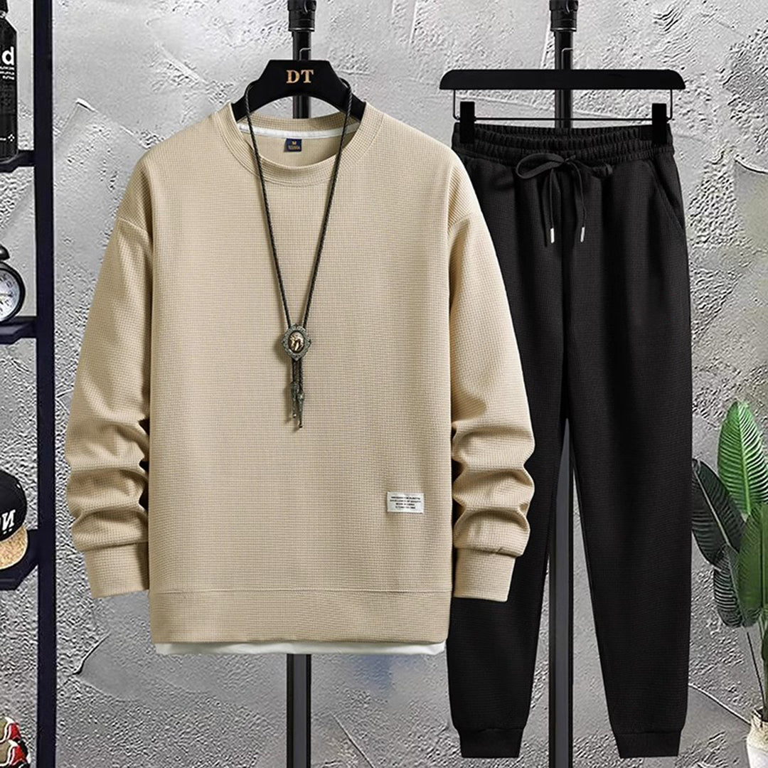 Heren joggingpak, beige trui en zwarte broek, casual sportkleding, comfortabele pasvorm, modieuze herenkleding, ideaal voor dagelijks gebruik.