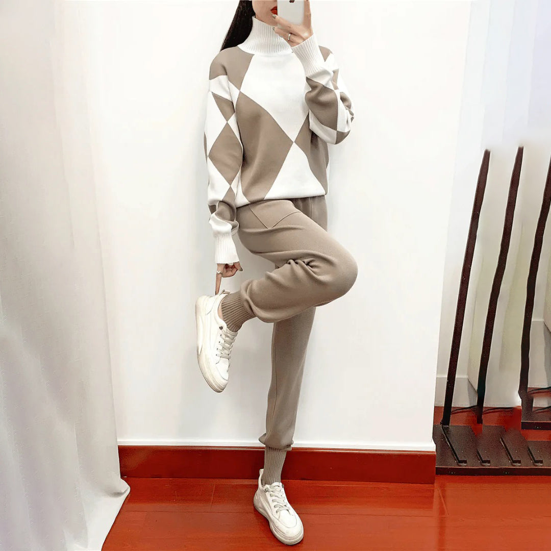 Vrouw in beige en witte trui met ruitpatroon en bijpassende broek, poseert op houten vloer. Modieuze dameskleding, comfortabele winterset.